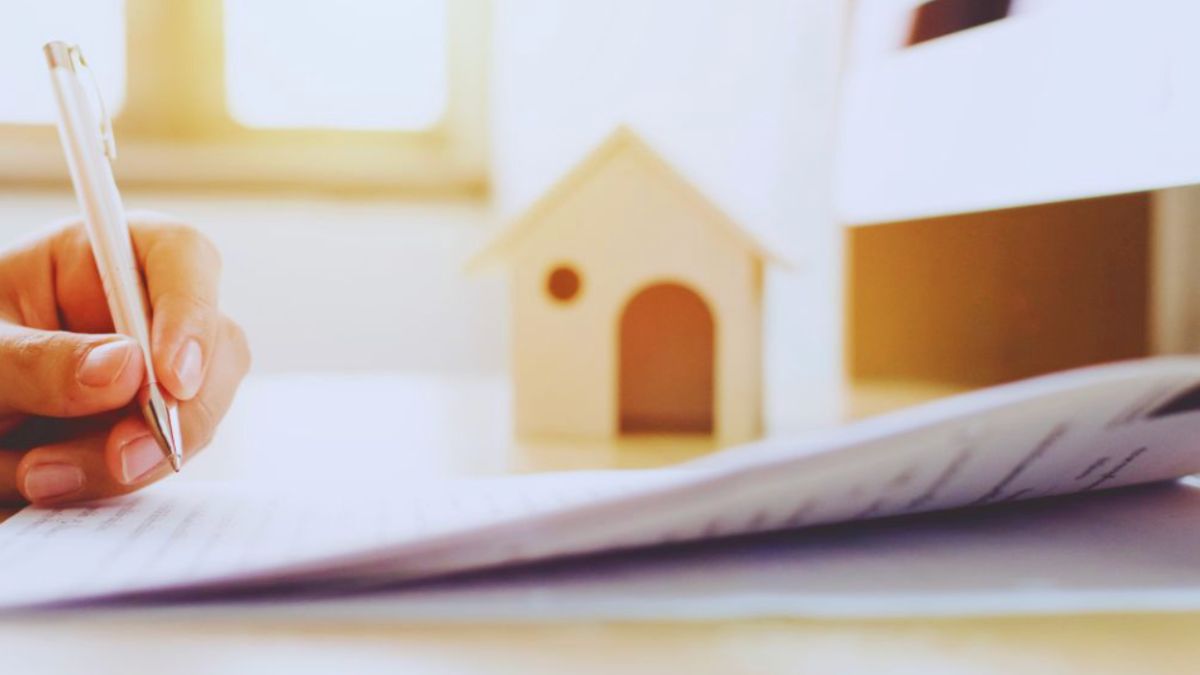 A person drafting a contract on paper with a pen, accompanied by a house model in the background, illustrating ownership rights.