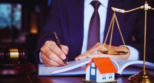A property dispute litigation lawyer in a suit writing in a legal document, with a gavel, scales of justice, and a small model house on the desk, symbolizing real estate legal services.