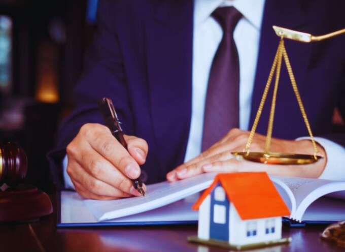 A property dispute litigation lawyer in a suit writing in a legal document, with a gavel, scales of justice, and a small model house on the desk, symbolizing real estate legal services.