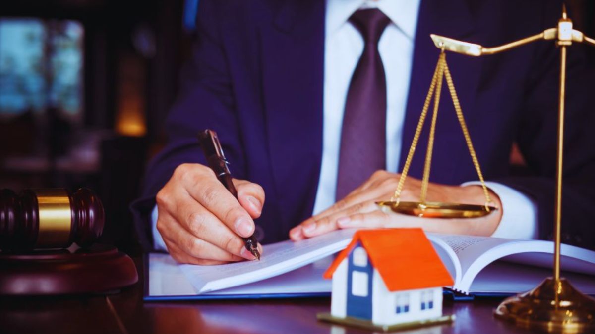 A property dispute litigation lawyer in a suit writing in a legal document, with a gavel, scales of justice, and a small model house on the desk, symbolizing real estate legal services.