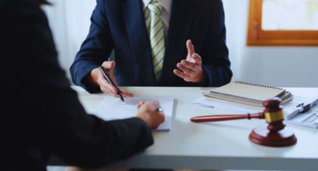 A contract lawyer in a business suit advises a client at a desk, reviewing a legal contract with a gavel and notebooks visible during a legal consultation.