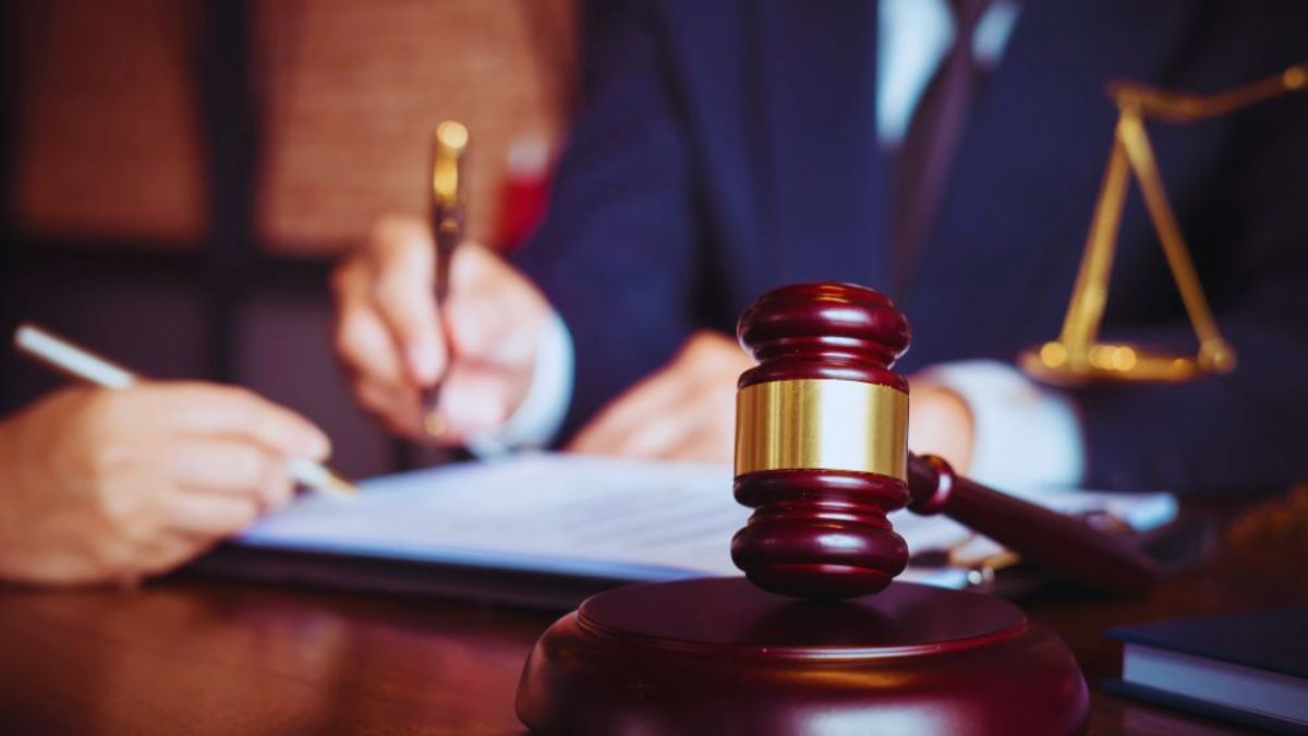 A contract lawyer in Hilton Head Island, SC, guides a client in signing a legal document at a desk; gavel and scales of justice are visible, highlighting contract and real estate matters.