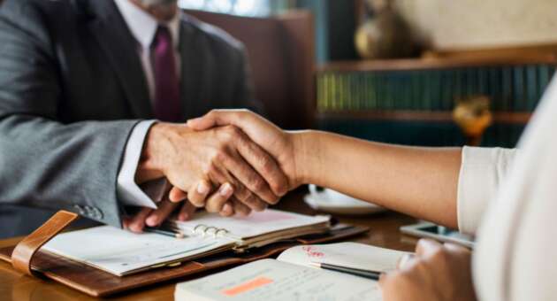 A real estate lawyer and a woman shaking hands at a desk, discussing property dispute solutions.