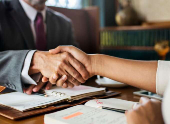 A real estate lawyer and a woman shaking hands at a desk, discussing property dispute solutions.