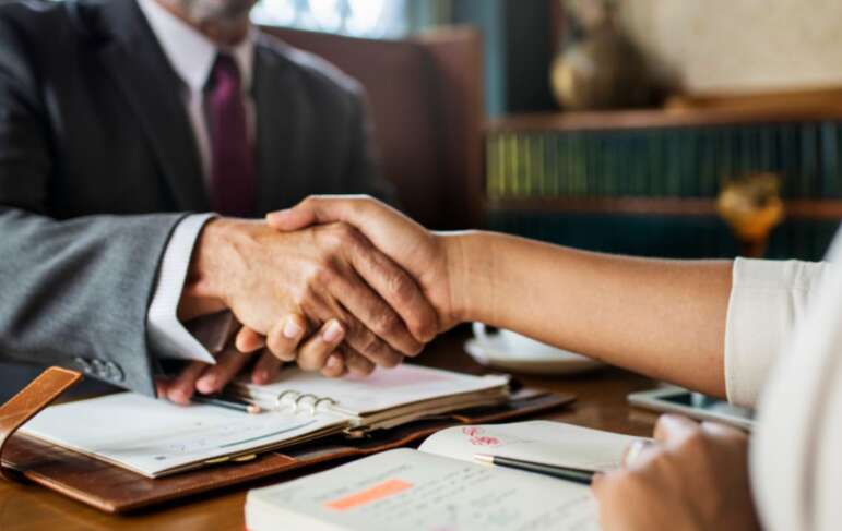 A real estate lawyer and a woman shaking hands at a desk, discussing property dispute solutions.