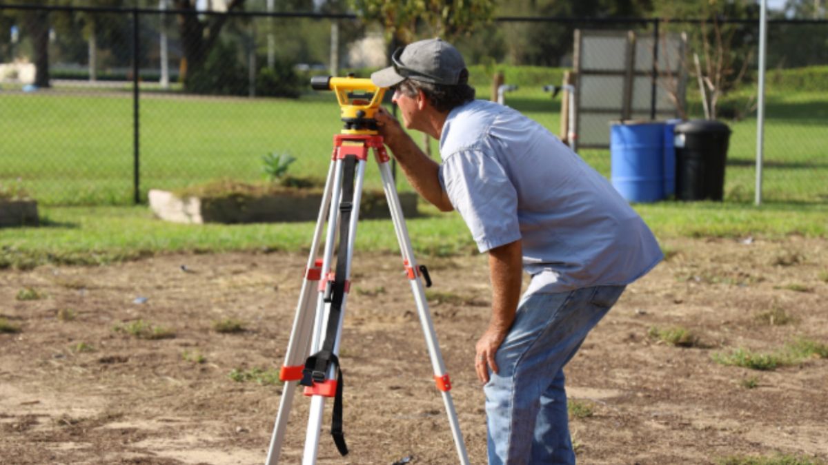 Land surveyor using a tripod-mounted instrument to verify residential property lines before purchase.