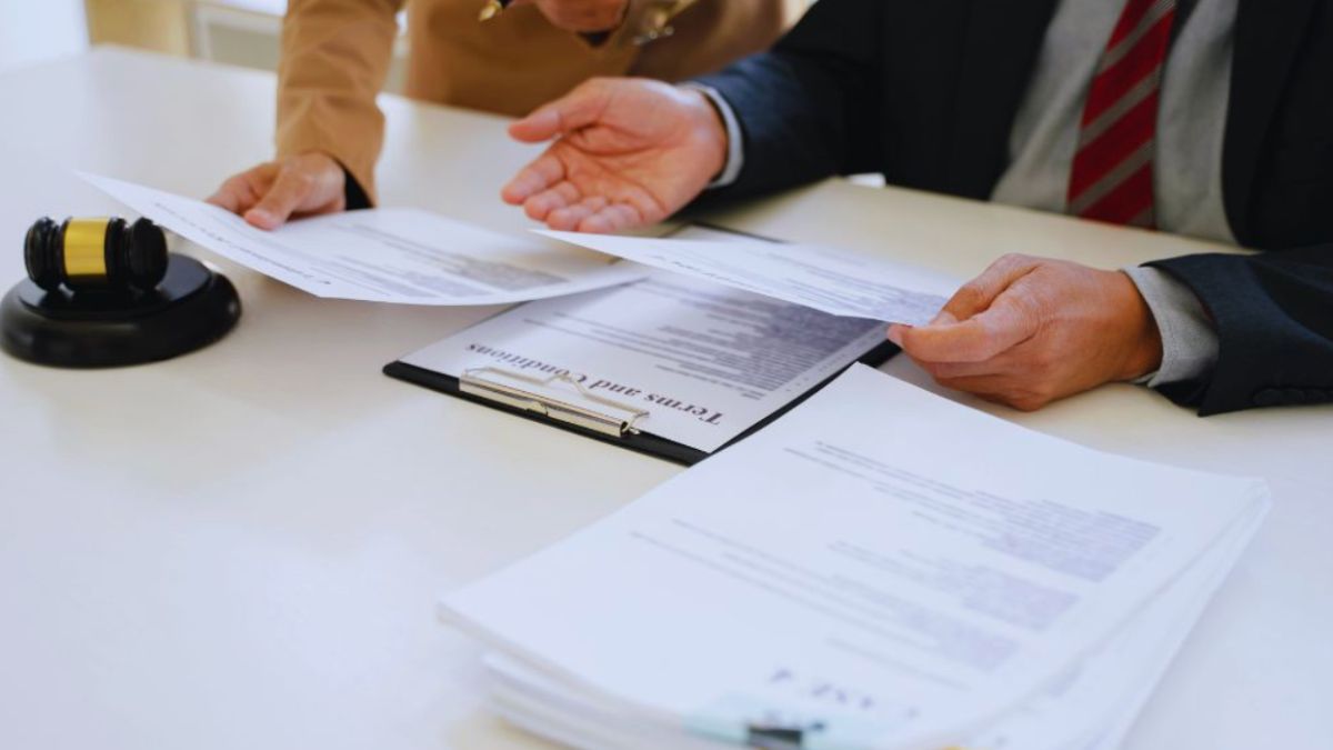 A lawyer guiding a client through contract law planning by carefully reviewing legal documents on a desk with a gavel, focusing on challenges such as keeping track of contract deadlines, renewal dates, compliance terms, and legal obligations to prevent disputes and enable smooth agreements.