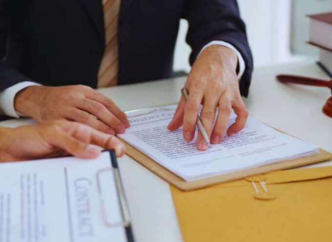Lawyer reviewing and explaining contract documents with a client during contract law planning, focusing on legal terms, obligations, and dispute prevention, with a gavel and legal books on the desk.