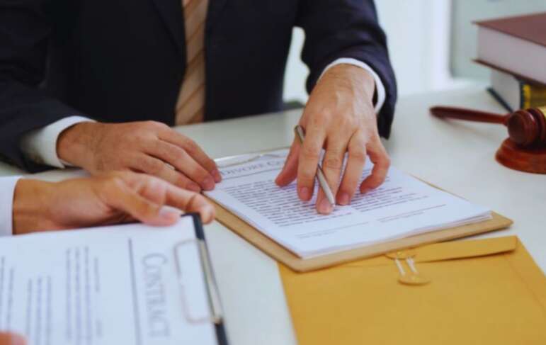 Lawyer reviewing and explaining contract documents with a client during contract law planning, focusing on legal terms, obligations, and dispute prevention, with a gavel and legal books on the desk.