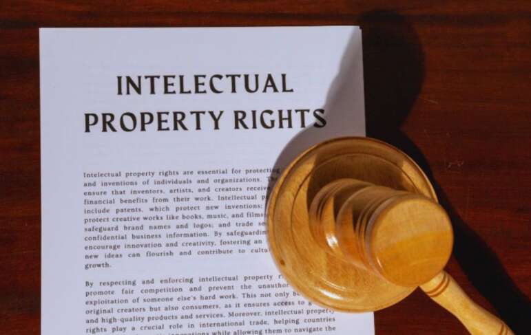 A document titled 'PROPERTY RIGHTS LAW' related to real estate ownership is displayed on a wooden surface, with a wooden judge's gavel resting on the lower right corner of the paper.