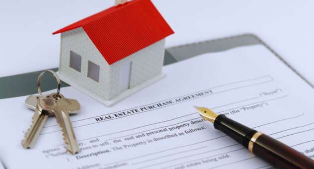 A real estate purchase agreement sits on a desk with a fountain pen, keys, and a model house, symbolizing the home-buying process.