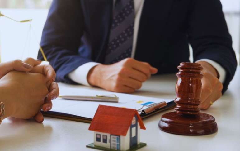 Attorney meeting with a client in Bluffton, SC, with legal documents, a gavel, and a house model representing wills, trusts, and asset planning.