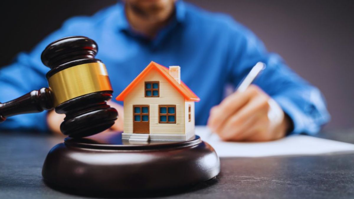 A real estate lawyer writing on documents at a desk with a judge’s gavel and a small model house in the foreground, symbolizing legal matters in property and real estate transactions.