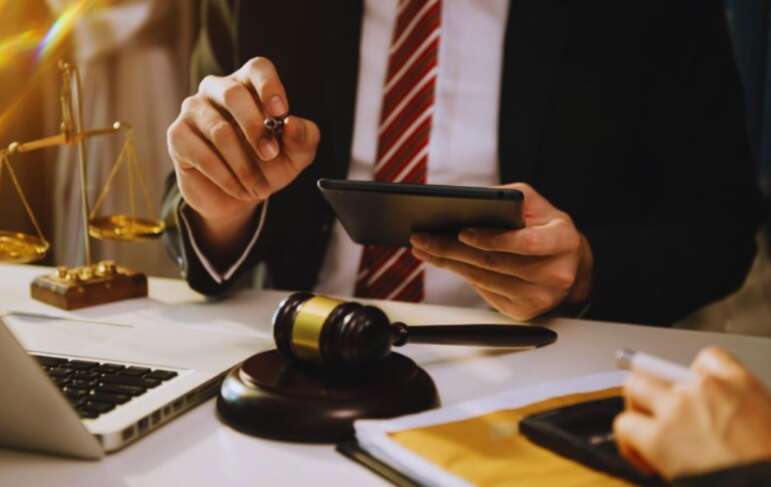 Construction law attorney in Bluffton at a desk with a gavel, laptop, tablet, and scales of justice, reviewing case documents and advising a construction client.