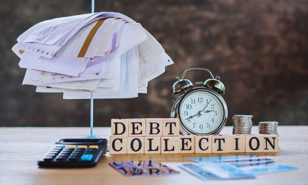 Stack of unpaid bills clipped together above a calculator, with a clock, coins, and blocks spelling “debt collection,” representing financial pressure and overdue payments.