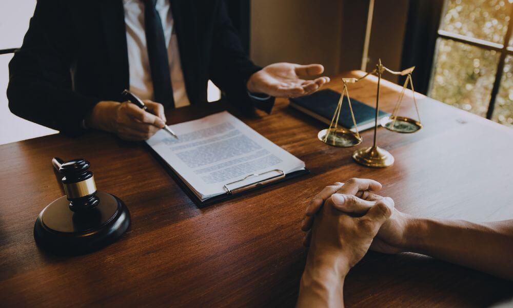 Collection attorney reviewing documents with a client at a desk, with a gavel and scales of justice nearby, discussing debt recovery and legal options.