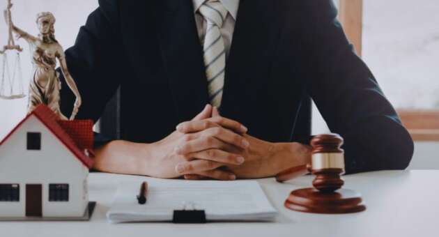 A real estate lawyer in a dark suit sits at a desk with hands clasped, framed by a small model house, legal documents, and a judge’s gavel, symbolizing South Carolina property law services.