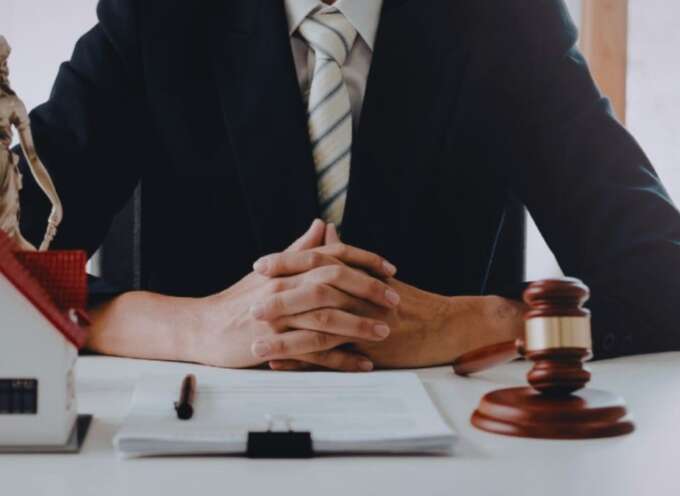 A real estate lawyer in a dark suit sits at a desk with hands clasped, framed by a small model house, legal documents, and a judge’s gavel, symbolizing South Carolina property law services.