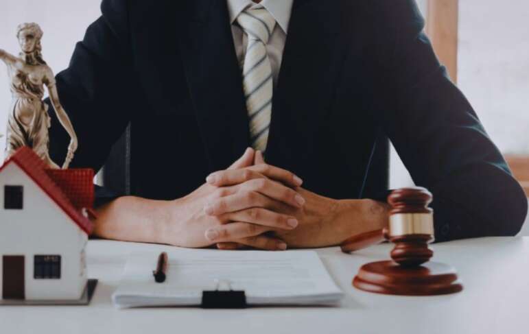 A real estate lawyer in a dark suit sits at a desk with hands clasped, framed by a small model house, legal documents, and a judge’s gavel, symbolizing South Carolina property law services.