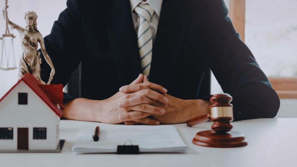 A real estate lawyer in a dark suit sits at a desk with hands clasped, framed by a small model house, legal documents, and a judge’s gavel, symbolizing South Carolina property law services.