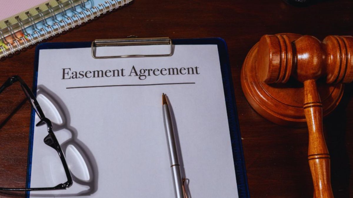 A wooden judge’s gavel rests beside a clipboard labeled “Easement Agreement,” with a pen and eyeglasses on a dark desk, illustrating a property easement legal issue in South Carolina.
