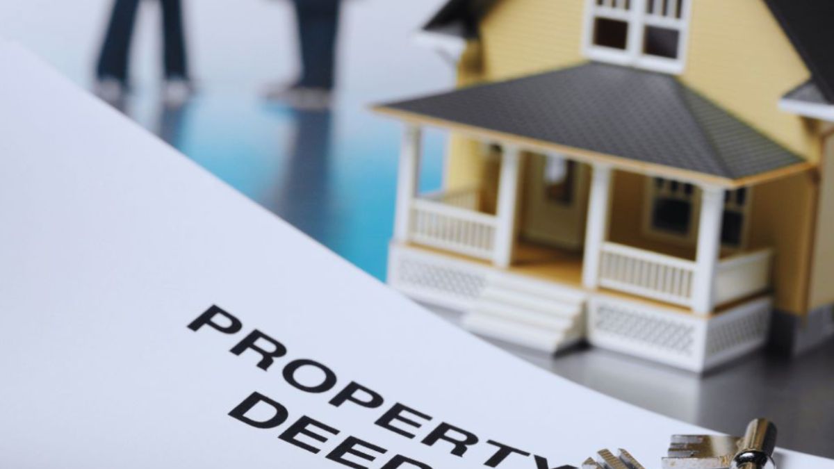 Close-up of a property deed document with house keys resting on it and a model house in the background, illustrating real estate title or ownership issues.
