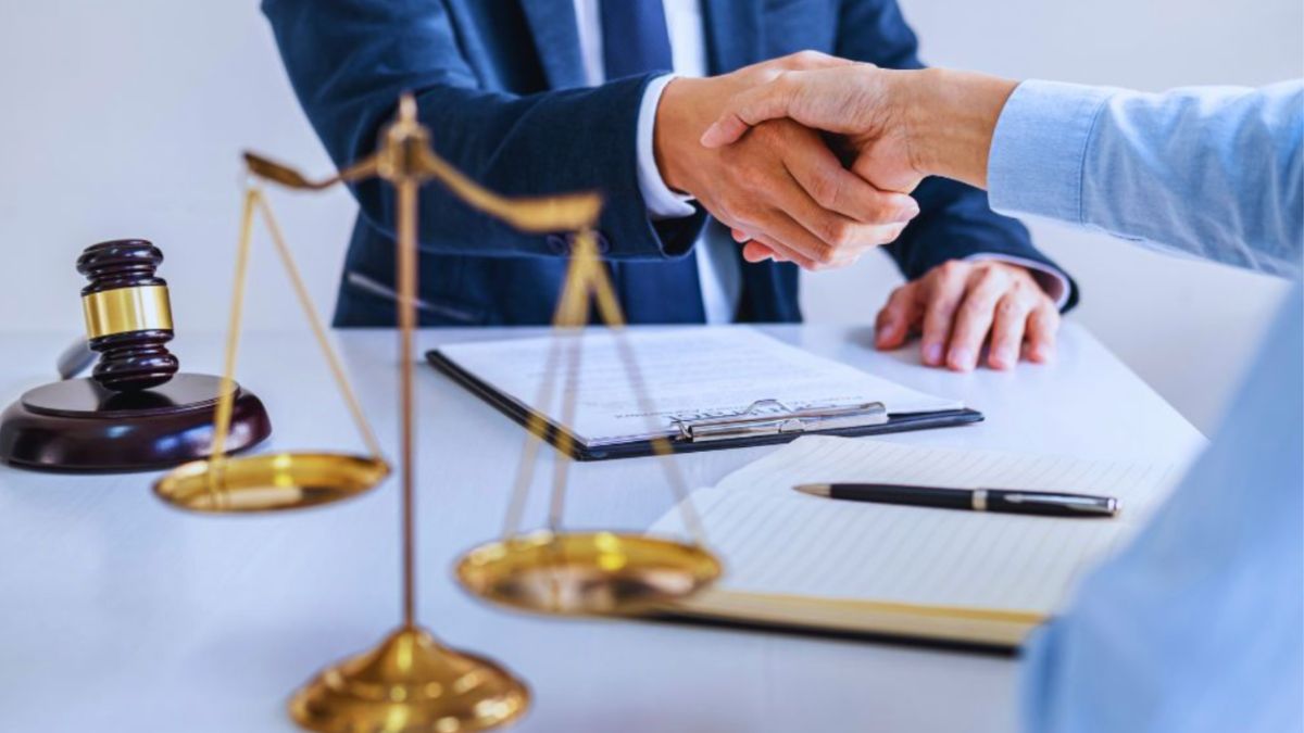 Contract lawyer and client shaking hands across a desk after reviewing legal documents.