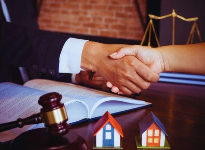 Close-up of an attorney and client shaking hands over an open legal document, with a judge’s gavel and two model houses on the desk, representing property dispute resolution in Hilton Head Island, SC