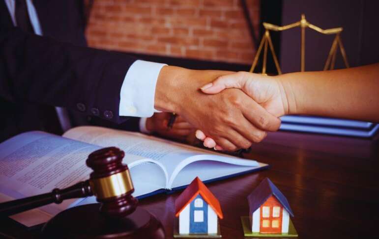 Close-up of an attorney and client shaking hands over an open legal document, with a judge’s gavel and two model houses on the desk, representing property dispute resolution in Hilton Head Island, SC