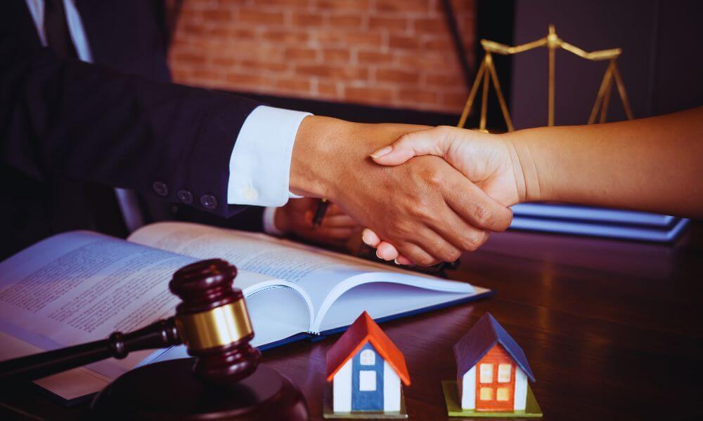 Close-up of an attorney and client shaking hands over an open legal document, with a judge’s gavel and two model houses on the desk, representing property dispute resolution in Hilton Head Island, SC