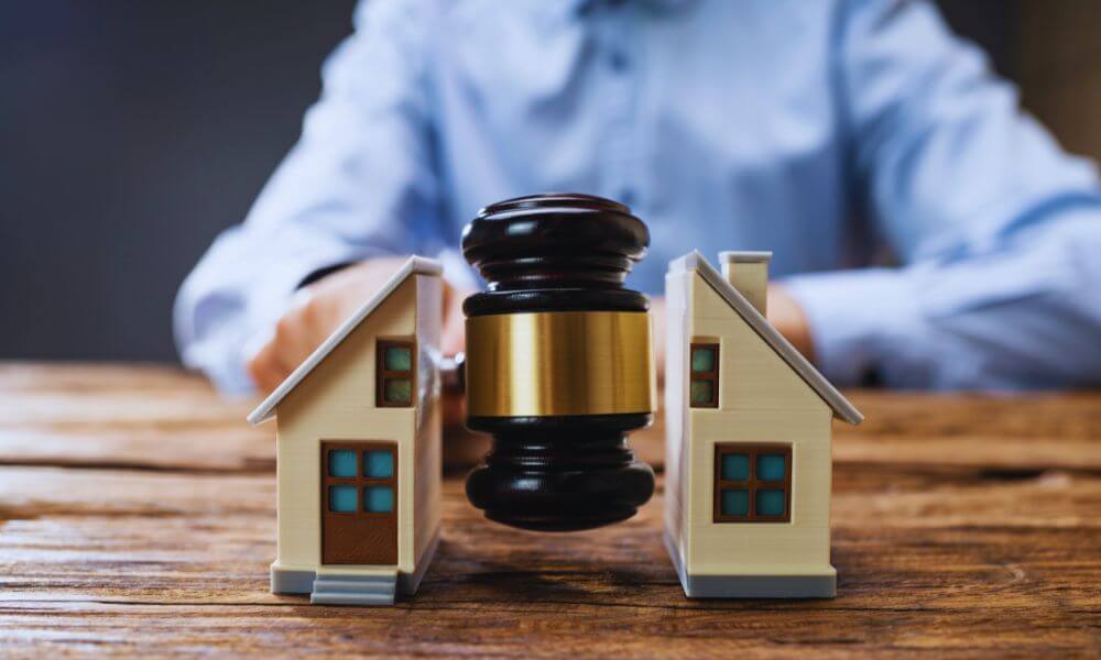 Two model houses on a wooden table with a judge’s gavel placed between them, symbolizing property disputes and real estate litigation services in Hilton Head Island, SC