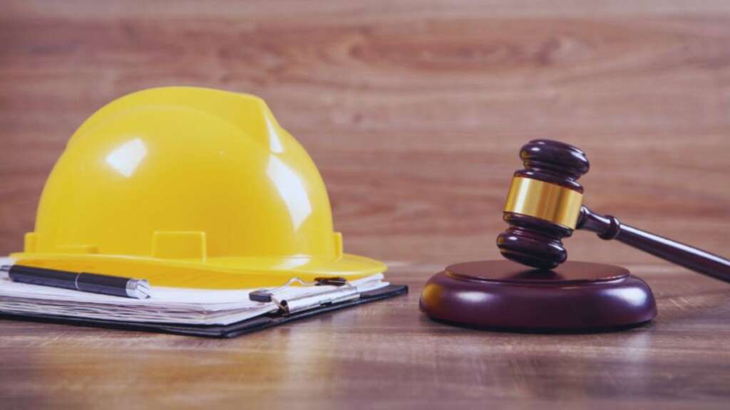 Construction accident lawyer concept showing a yellow construction hard hat on documents beside a judge's gavel, symbolizing legal representation for injured construction workers and workplace accident claims.