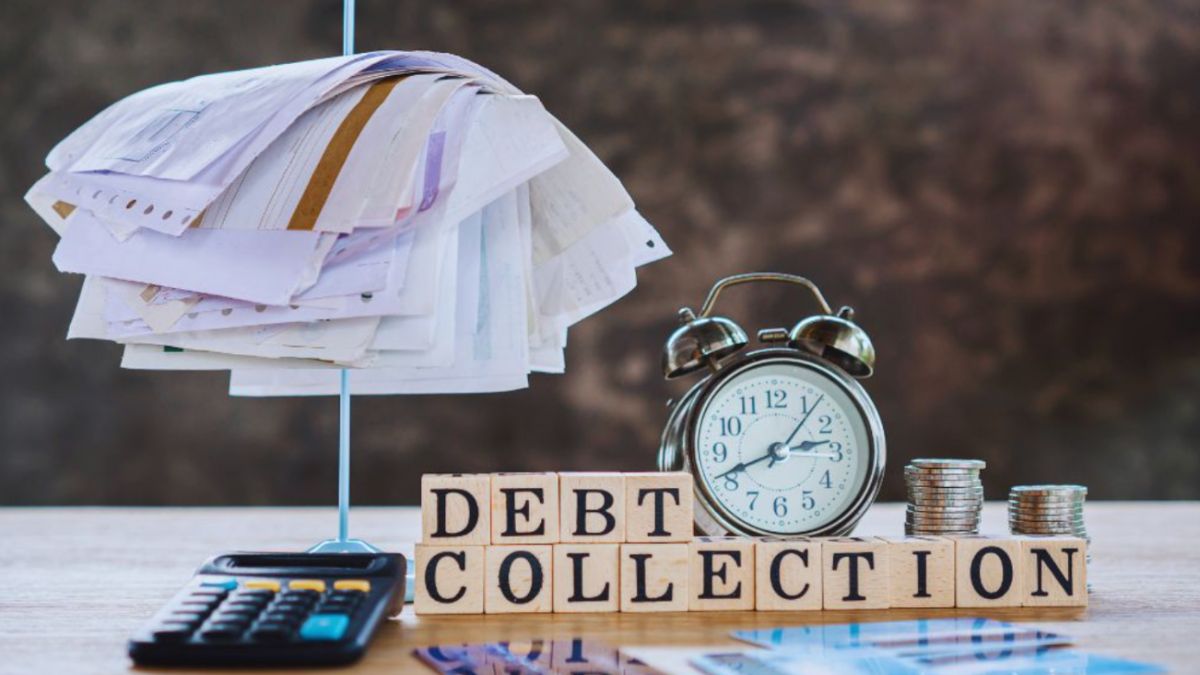 Stack of unpaid bills clipped together above a calculator, with a clock, coins, and blocks spelling “debt collection,” representing financial pressure and overdue payments.